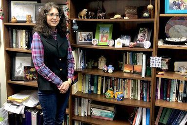 一位女教授站在摆满书的书柜前, photos, and different memorabilia 