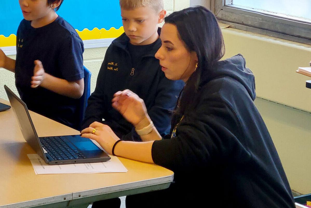 A student teacher helps a student on a laptop